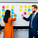 A diverse group of professional men and women, fully clothed in modest business suits and appropriate attire, actively collaborating in a bright, modern office space. They are gathered around a large whiteboard covered with colorful sticky notes, engaged in a dynamic brainstorming session. Some are writing, others are discussing, demonstrating teamwork and an agile mindset. The atmosphere is energetic and innovative. The background features contemporary office furniture and large windows with soft natural light. safe for work, appropriate content, fully clothed, professional, family-friendly, perfect anatomy, correct proportions, natural pose, well-formed hands, proper finger count, natural body proportions, professional photography, high quality.